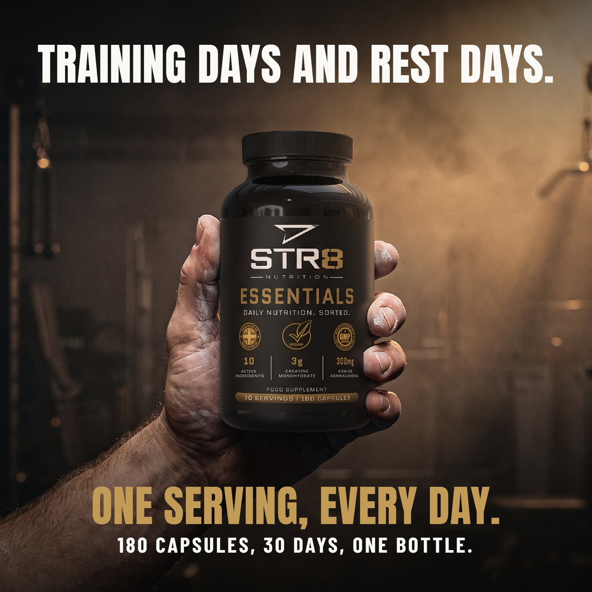 A hand holding a bottle of STR8 Nutrition Essentials in a gym. Training days and rest days. One serving, every day. 180 capsules, 30 days, one bottle.